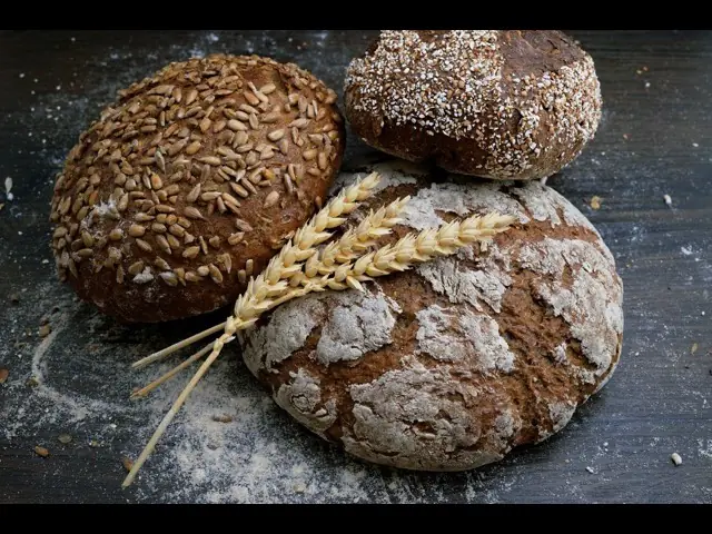 Three seeded and floured loaves cooling on a dark surface.